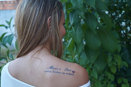 woman wearing white boat-neck top in front of green leafed plants thumbnail