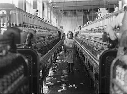 grayscale photo of girl standing between industrial sewing machine thumbnail