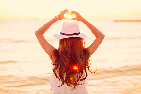 woman in white fedora hat, white sleeveless top standing near body of water thumbnail