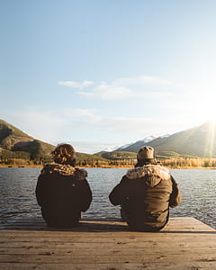 two persons sitting on dock overlooking body of water thumbnail
