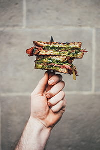 Gourmet pesto sandwich held with knife in a hand thumbnail
