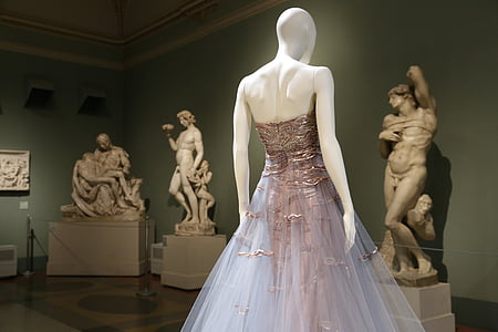 white mannequin wearing gown facing statues thumbnail