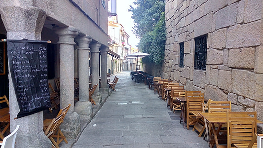 brown wooden tables and chairs on pathway between two buildings thumbnail
