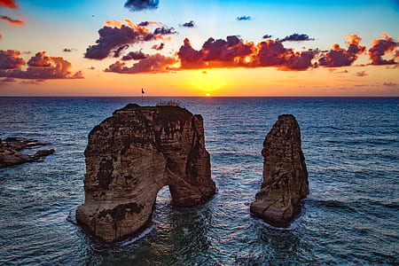 two brown rock formations on body of water under blue cloudy skies golden hour photography thumbnail