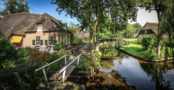 photograph of brown concrete house near green leaf tree beside body of water thumbnail