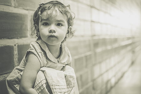 grayscale photo of girl sitting against brick wall thumbnail