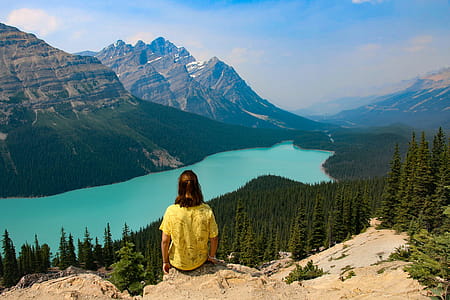 Person Sitting on Rocky Mountain Near Body of Water thumbnail