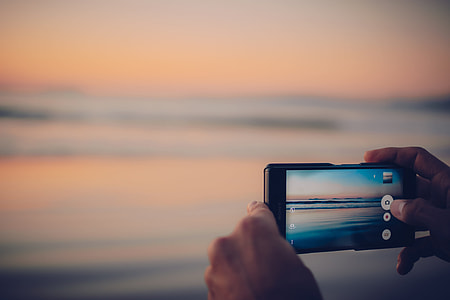 person holding camera taking photo of shore thumbnail