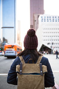 woman carrying brown leather backpack facing high rise buildings thumbnail