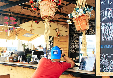 Man Near Counter Desk With Hanging Surfboard thumbnail