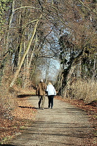 man and woman wearing jackets walking on pathway between trees thumbnail