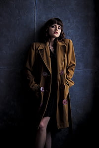 woman wearing brown trench coat stands next to blue painted wall thumbnail