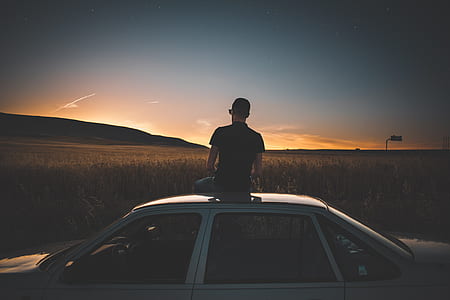 man wearing black shirt sitting on top of white sedan near wheat field thumbnail