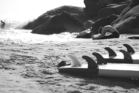 Grayscale Photo of Woman Sitting on Beach Near Rock Formation thumbnail