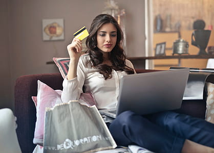 Young Adult woman using her credit card to shop online while holding laptop on her lap thumbnail