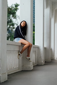 woman wearing black and white sweater while sitting on concrete fence during daytime thumbnail