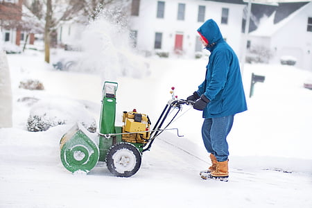 man wearing blue hooded jacket holding green snow thrower thumbnail