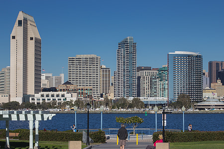 man walking towards body of water near high-rise building during daytime thumbnail