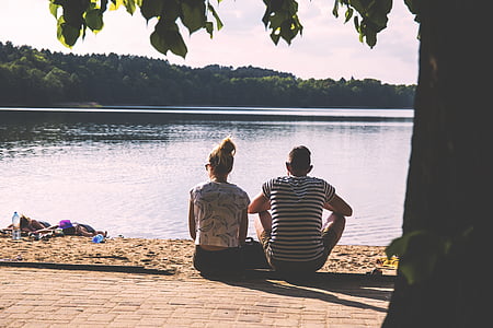 couple sitting on concrete floor front of body of water thumbnail