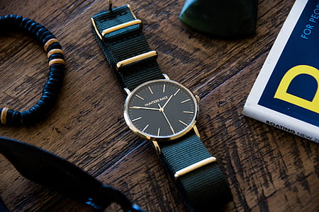 round gold-colored analog watch with black leather strap beside black bracelet thumbnail