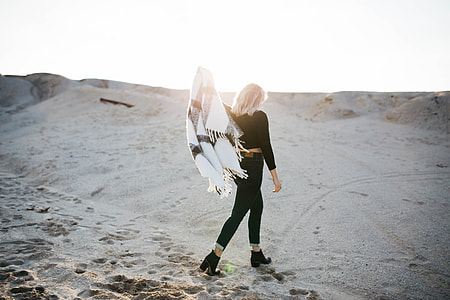 woman holds white scarf while walking on sand during daytime thumbnail