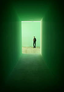 man wearing black jacket and blue jeans standing at the end of the hallway thumbnail