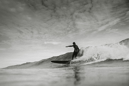 grascale photo of man surfing under cloud thumbnail