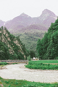 white metal bridge beside body of water and mountain thumbnail