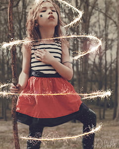 girl wearing black, white, and orange striped sleeveless dress surrounded by trees with yellow light effects thumbnail