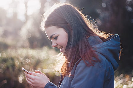 depth of field photography of woman wearing hoodie holding smartphone thumbnail