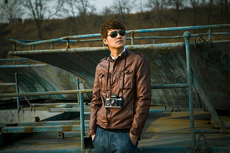 man wearing brown leather jacket near blue metal fence thumbnail
