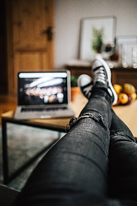 Woman in ripped jeans and black sneakers with a silver laptop on a wooden table thumbnail