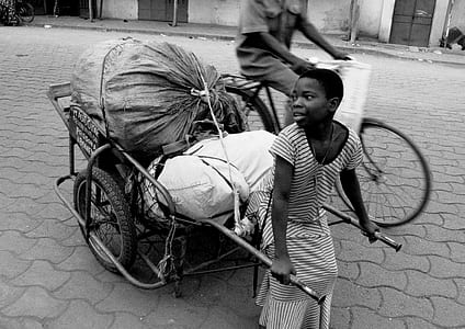 grayscale photo of boy pulling cart near man riding on bicycle during daytime thumbnail