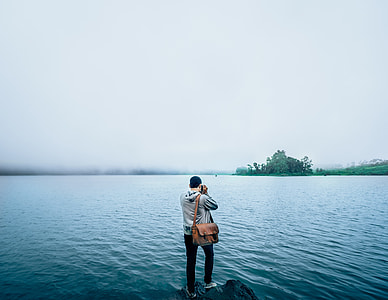man in grey hoodie standing on rock formation near body of water during daytime thumbnail