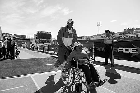 grayscale photography of man pushing woman in wheelchair thumbnail