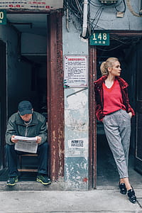 woman standing in front of door and man sitting while reading newspaper thumbnail