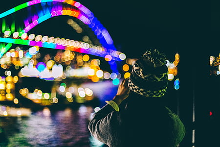 person standing in front of lighted bridge across large body of water during daytime thumbnail