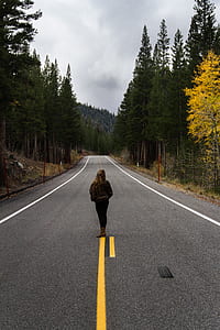 woman on middle of road between trees thumbnail