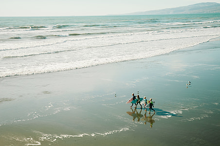 four person holding surfboard walking towards ocean thumbnail