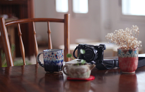 selective focus photograph of DSLR camera near mug and pot on wooden table thumbnail