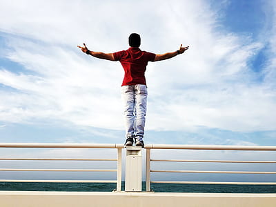 Person Raising Hands Mid-air Sidewards While Standing on Gray Steel Railings thumbnail