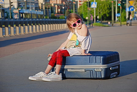 girl sitting on gray hardshell luggage on gray concrete road thumbnail