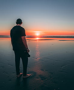 Man Standing on Beach during Sunset thumbnail