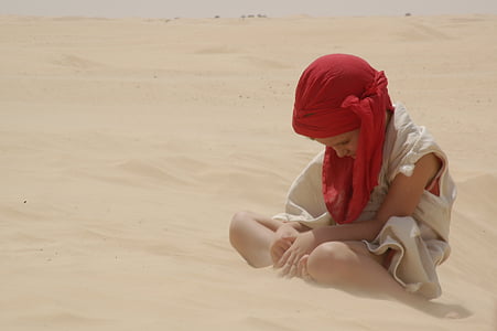 boy sitting on brown sand wearing white top thumbnail