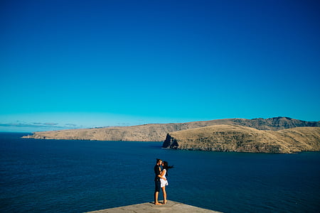man and woman kissing on ledge near body of water thumbnail