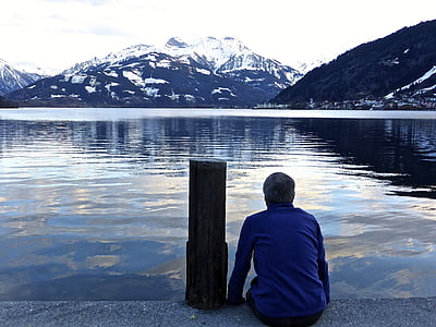 man sitting beside bollard facing body of water thumbnail