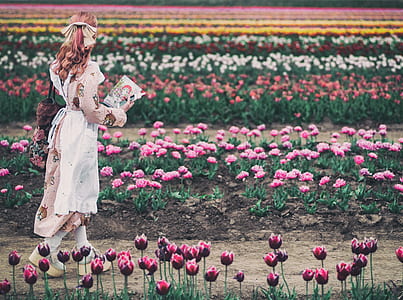 woman walking between flower field during daytime thumbnail