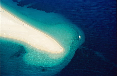 aerial photography of boat near islet thumbnail