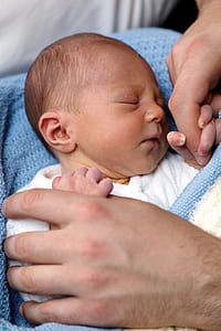 newborn covered with blanket beside hands thumbnail