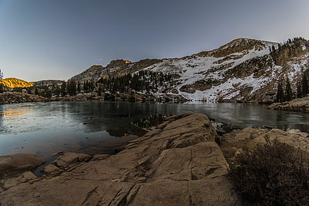 body of water beside brown and white mountain under clear blue sky thumbnail